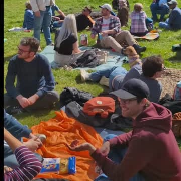 People talking in a circle on the grass, bikes and trees behind